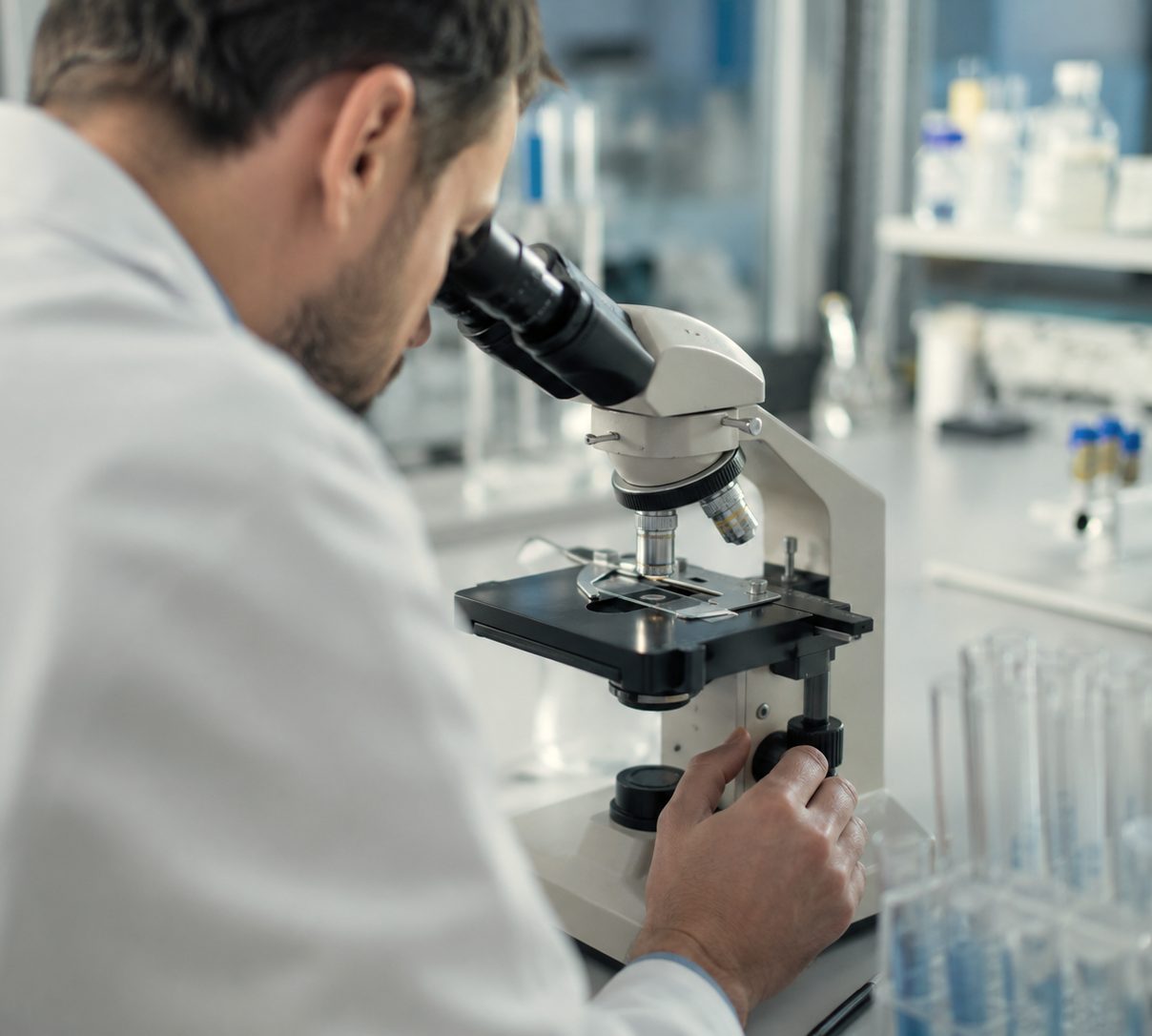 A researcher in a white coat examining a slide under a light microscope in a laboratory.